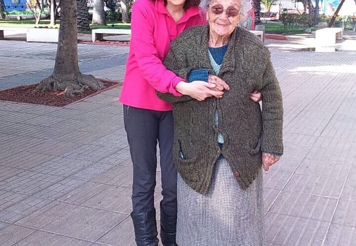 mujer junto a adulta mayor sonriendo en una plaza