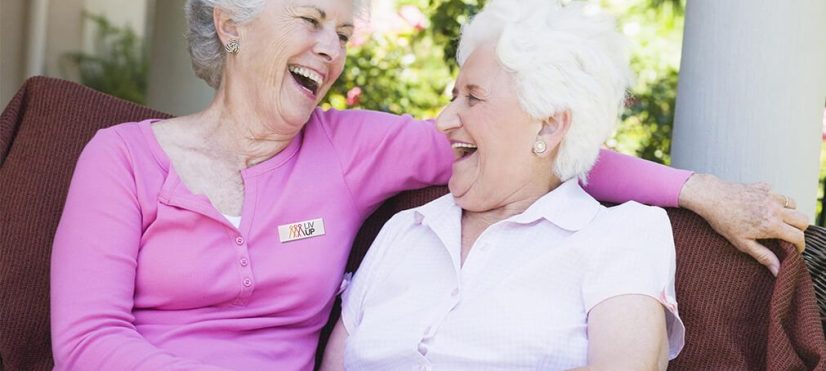 Pareja de adultas mayores riendo sentadas en una banca en el jardín